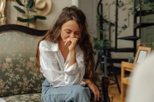 Woman in a white shirt sitting thoughtfully on a vintage sofa indoors.